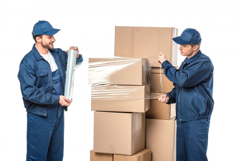 two movers wrapping cardboard boxes with roll of stretch film isolated on white